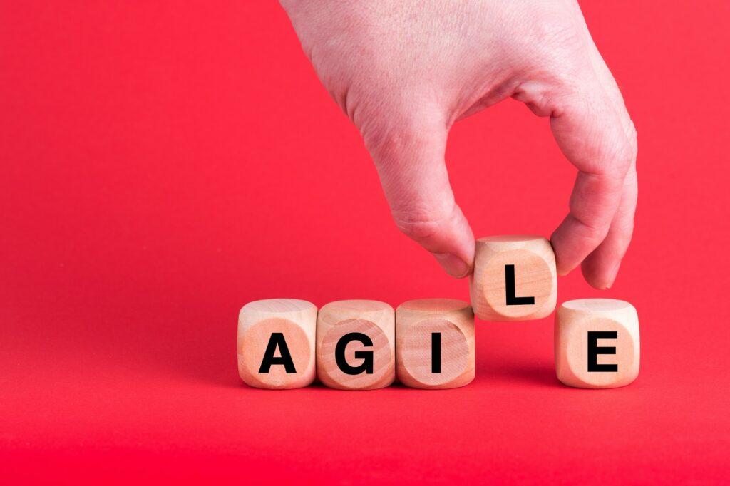 Closeup of someone arranging dices to read AGILE, on a red background