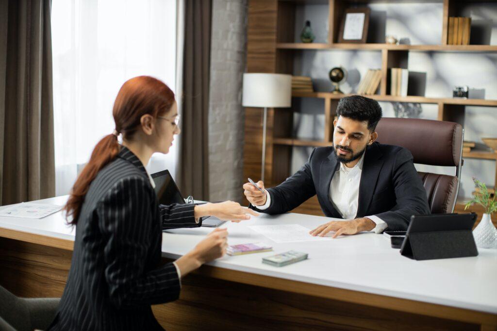 Confident businessman in black suit gives a salary to young red hair. Holiday Pay for Salaried Employees