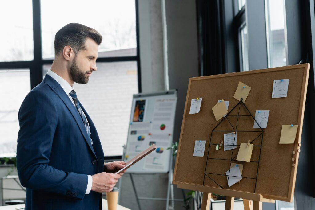 side view of economist with folder near corkboard with sticky notes and blurred flip chart